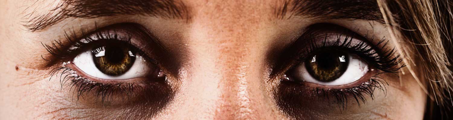 Cropped close up of a woman's sad, exhausted brown eyes, ringed with dark circles and looking straight at the camera